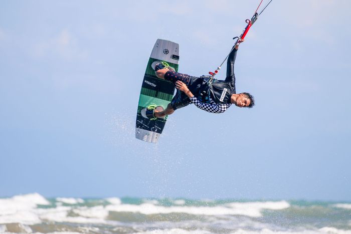 A man performing a stunning aerial trick while kitesurfing in the ocean on a sunny day.