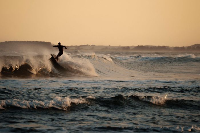Silhouetted surfer carving through waves at sunset with warm tones and an ocean backdrop.