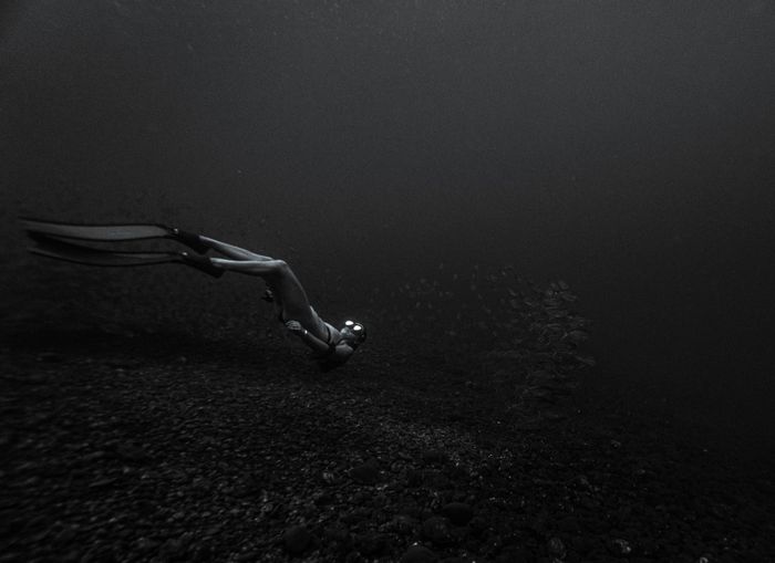 A lone diver explores the depths in a monochromatic underwater scene, showcasing tranquility and exploration.