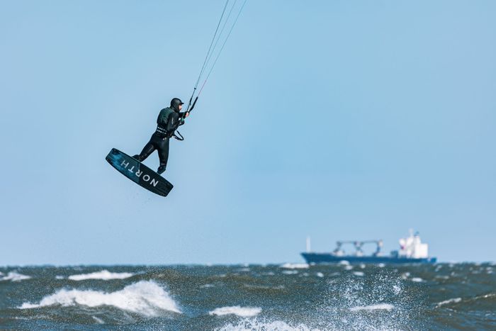 Kitesurfer leaps high above ocean waves under blue sky, showcasing extreme water sports action.