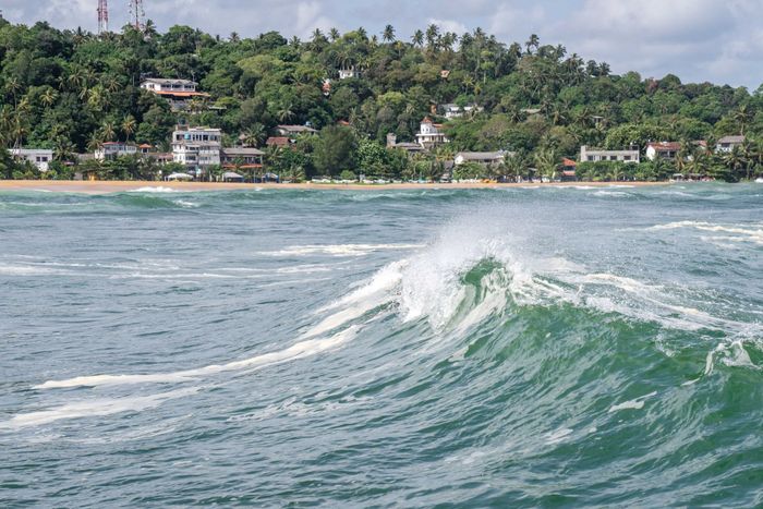 Vivid ocean waves crashing against the picturesque coastline of Unawatuna, Sri Lanka. Lush greenery in the background.