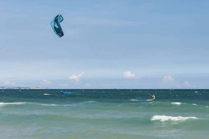 Dynamic kitesurfing scene with clear blue skies and ocean waves.