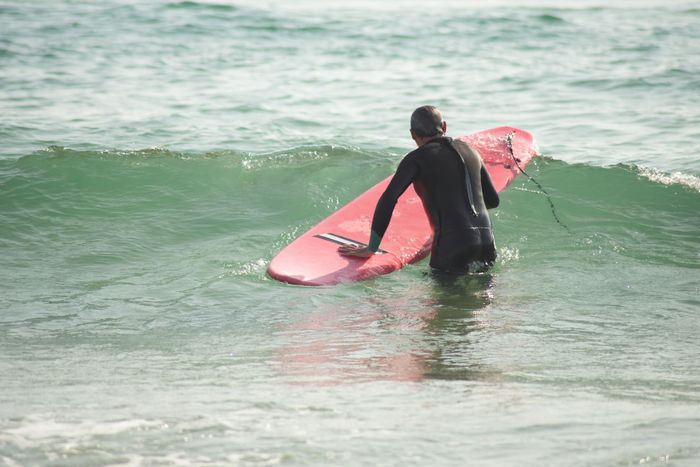 A surfer in a wetsuit with a red surfboard heading into the ocean waves at a Portuguese beach.