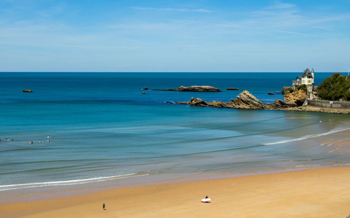 Beautiful view of Côte des Basques beach in Biarritz, France with surfers and clear blue water.