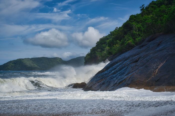 Majestic coastal view of waves crashing against rocky shores in Ubatuba, Brazil, under a clear blue sky.
