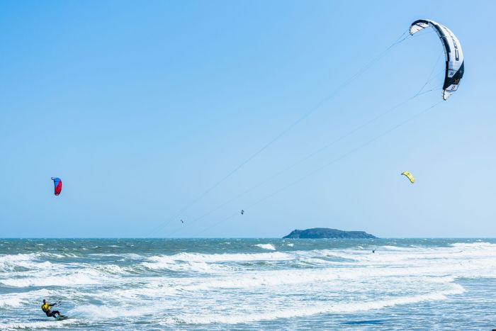 Dynamic kitesurfing action with a clear blue sky and ocean waves, perfect for adventure travel enthusiasts.