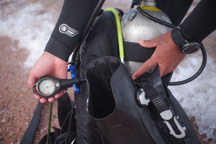 A scuba diver adjusts their gear on a sandy beach, ready for diving adventure.