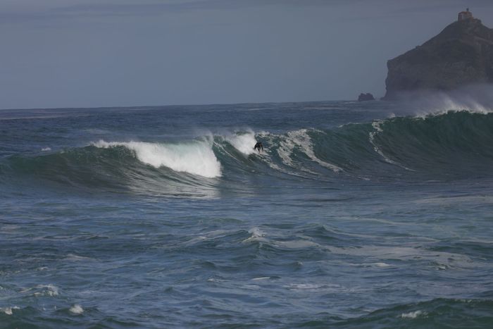 Surfer skillfully rides a wave on a rugged coastline, capturing the thrill of ocean surfing.