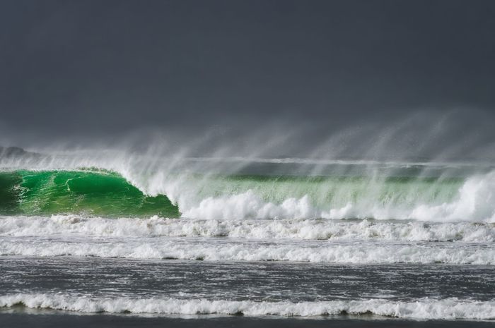 Powerful waves crashing on a beach in Ireland under a dark sky, capturing the ocean's dynamic energy.