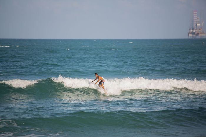 A young man skillfully surfs a wave in the ocean under a clear blue sky.