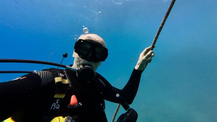 A scuba diver grips a rope underwater, surrounded by clear blue sea.
