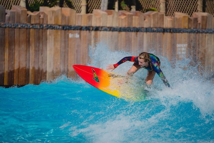 Dynamic image of a woman surfing a wave on a colorful surfboard in an outdoor pool.