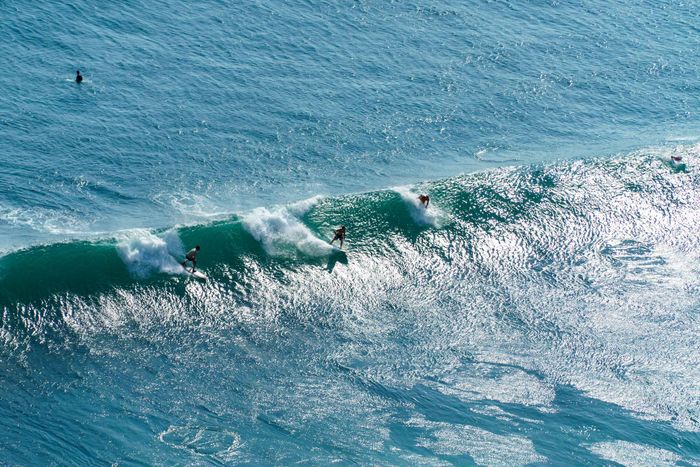 Aerial shot of surfers riding vibrant waves in Bali, Indonesia's clear blue waters.