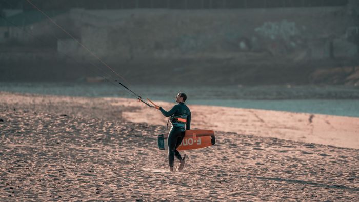 A kitesurfer carrying equipment on a sandy beach during dusk in Spain, capturing a serene moment.