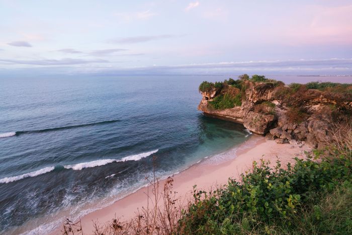 Scenic view of sandy Balangan Beach with famous wedding cliff and calm blue ocean under magnificent tenderly colored sky