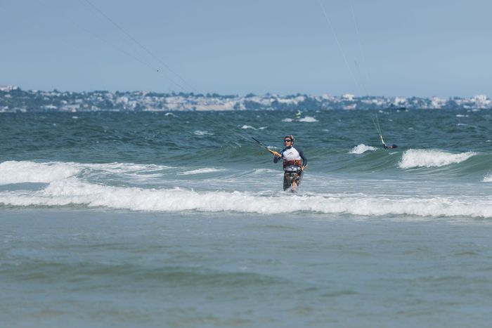 A kitesurfer stands confidently in the waves, ready for adventure on a sunny beach day.
