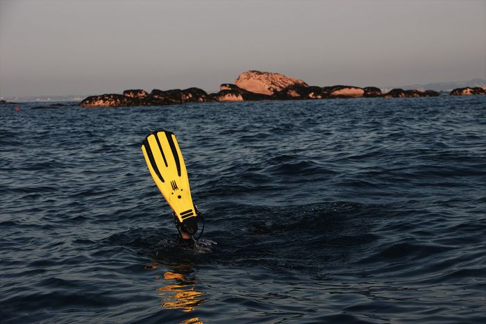 A diver in ocean waters with prominent yellow flippers, exploring near rocky islands.