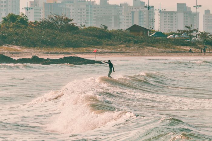 A lone surfer skillfully rides waves on a Brazilian beach with a city backdrop, capturing the essence of coastal adventure.