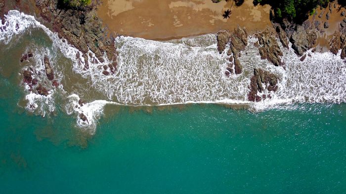 Stunning aerial shot of waves crashing on a rocky beach in Costa Rica's lush landscape.