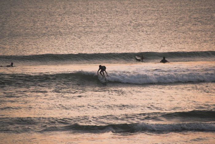 A surfer rides the waves during a stunning sunset on a Bali beach, showcasing water sports excitement.