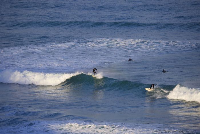 Surfers riding waves on a clear day at Watergate Bay in Cornwall, UK.