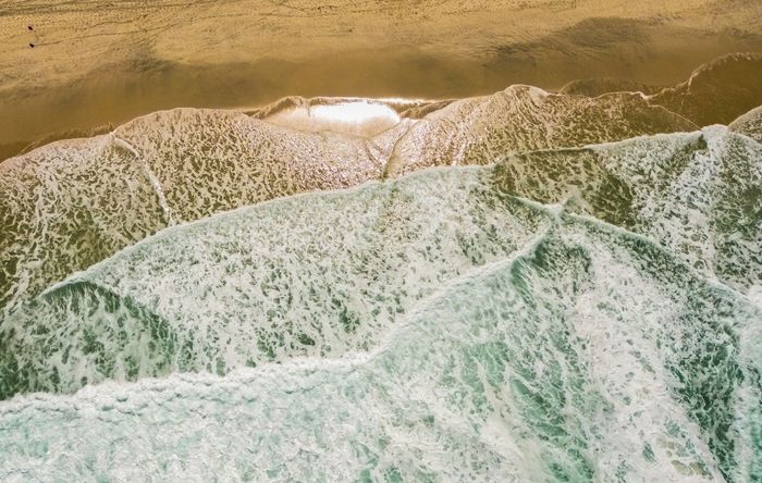 A stunning aerial shot capturing turquoise waves meeting the golden sands of Rio's Praia da Barra beach.