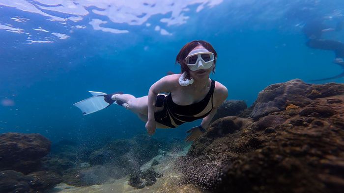 Explore serene underwater world with a woman snorkeling near vibrant coral reefs.