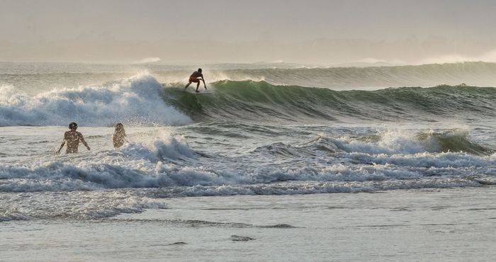 Surfer riding waves at sunset on a Bali beach, Indonesia. Perfect for travel and adventure imagery.