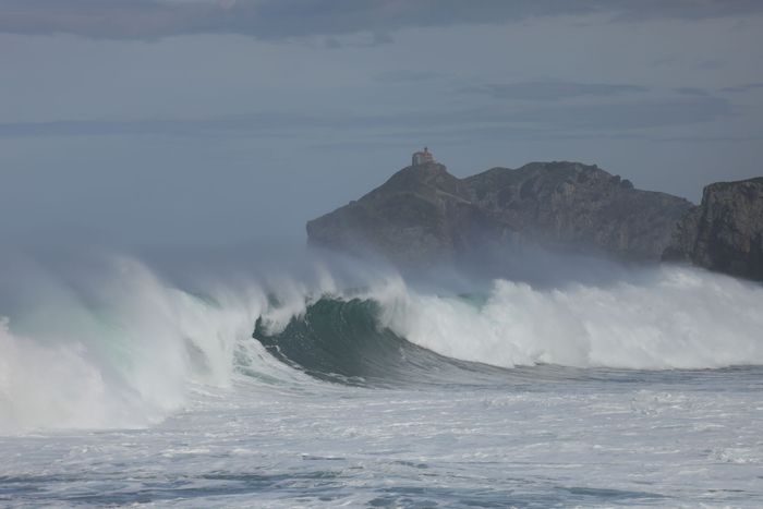 Powerful ocean waves crashing onto Bakio's rugged coastline under cloudy skies.