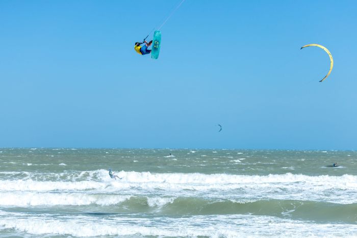 Kitesurfer executing a dramatic aerial stunt over ocean waves under a clear blue sky, showcasing extreme sports action.