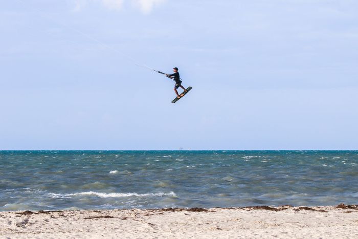A kitesurfer jumps high above the waves at Mayapo Beach, Colombia, showcasing extreme skills.