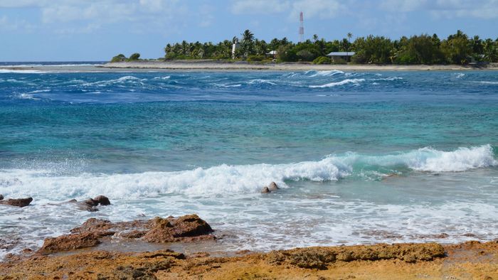 Vibrant tropical beach with clear waves and rocky shore under a blue sky.