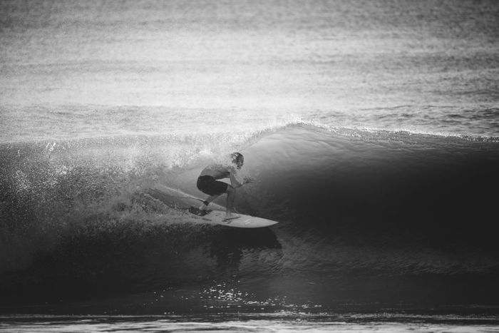 Black and white photo of a surfer riding a wave, capturing the thrill of surfing at sea.