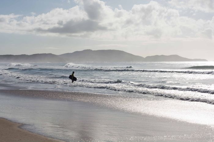 Bodyboarder on a picturesque Cabo Frio beach with waves and cloudy sky.