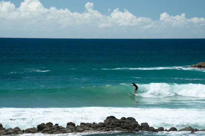 A surfer expertly rides a wave against a backdrop of a sunny beach and blue skies.