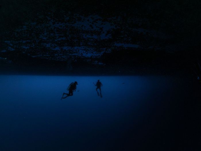 Two scuba divers exploring deep underwater with dramatic silhouettes, evoking mystery and adventure.