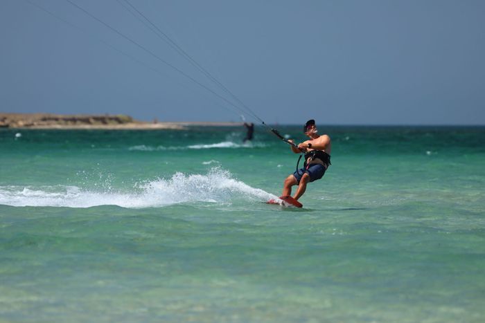 Shirtless man kiteboarding on turquoise waters, capturing the thrill of the sport.