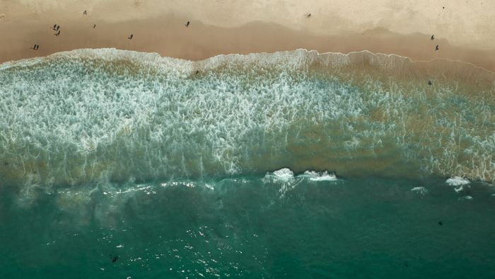 Breathtaking aerial shot of Cape Town's beach with crashing waves and surfers.