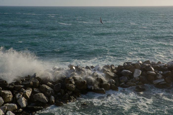 A scenic view of ocean waves crashing against rocky shores under a bright sky in Italy.