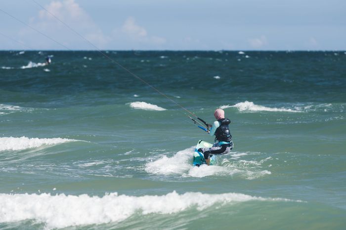 A woman enjoys kitesurfing over crashing ocean waves on a sunny day.