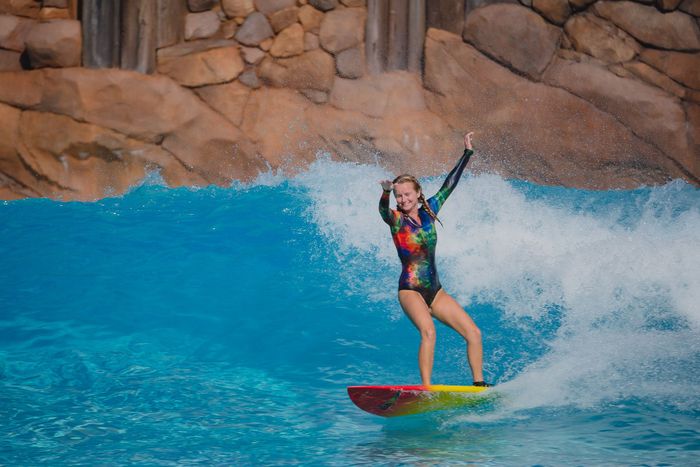 Enjoy the thrill of surfing on an artificial wave with vibrant sportswear in a pool setting.