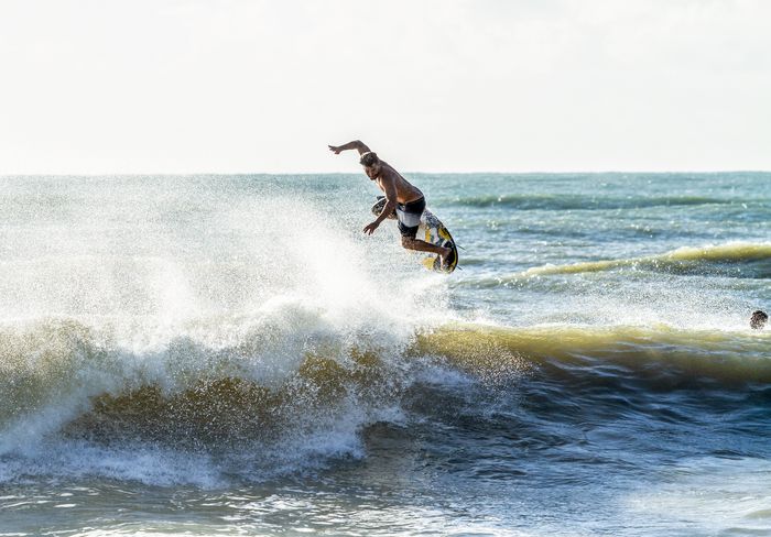 A surfer in mid-air performs an impressive maneuver against stunning ocean waves at Baía Formosa.