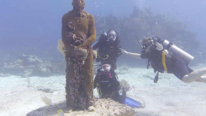 Divers exploring an underwater museum in Isla Mujeres, capturing marine life art.