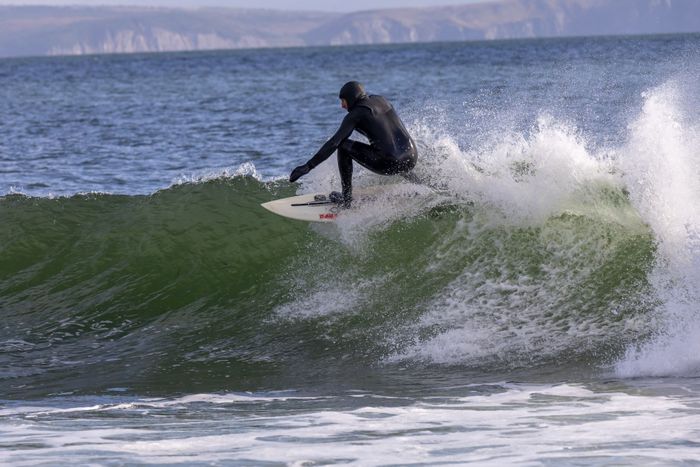 A surfer in wetsuit skillfully rides a wave on a cool day at the ocean.