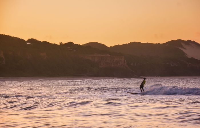 Surfer riding waves at sunset in RN, Brazil's scenic coastline. Perfect for adventure and travel themes.