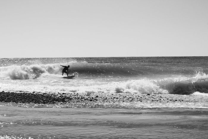 Dynamic black and white image of a surfer riding waves at the beach in Sochi, Russia.