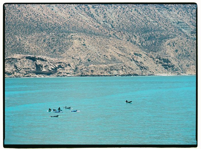 Surfers paddle on clear waters near rocky coast in Morocco. Perfect for water sports.