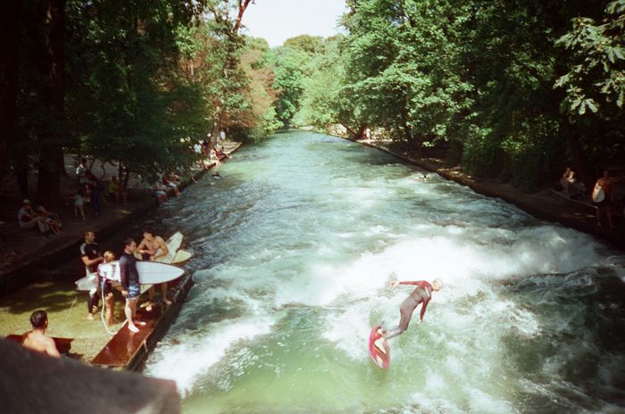 Surfers ride artificial waves on a river in Munich's English Garden.
