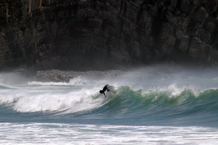 Surfer riding waves against a rocky coastline, showcasing exhilarating ocean sport.