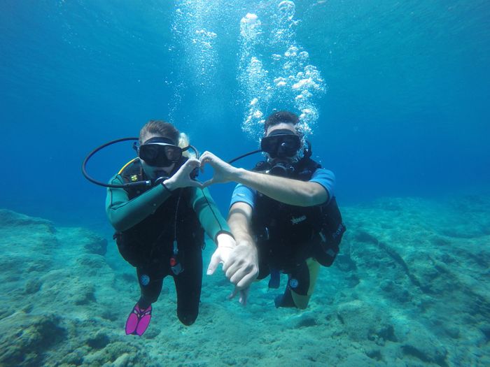 A couple creating a heart shape while scuba diving in crystal clear seawater, enjoying an underwater adventure.